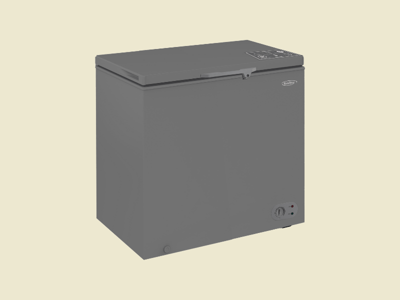 Grey compact chest freezer with a top opening lid and a thermostat dial on the lower right set against a pale beige backdrop