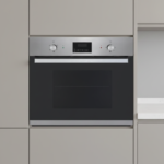 Built in stainless steel oven set in light gray kitchen cabinetry with a black glass door and control panel above the door